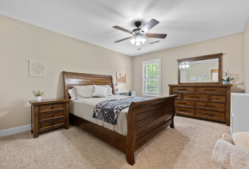 Bedroom featuring neutral wall paint, light-colored carpet, a ceiling fan with integrated lighting, and a window with white plantation shutters