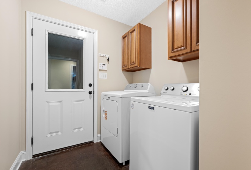Dedicated laundry area featuring a white paneled door with a clear glass insert, rich wood-finish cabinetry, and neutral wall tones