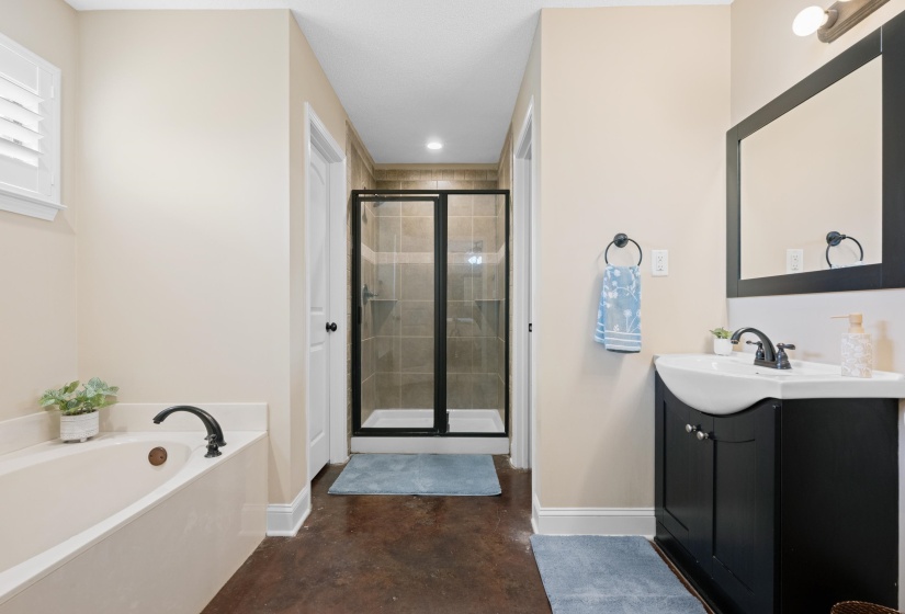Bathroom featuring a soaking tub with dark-finish fixtures, a separate shower with glass enclosure, and a vanity with a white vessel sink and dark-finish cabinet