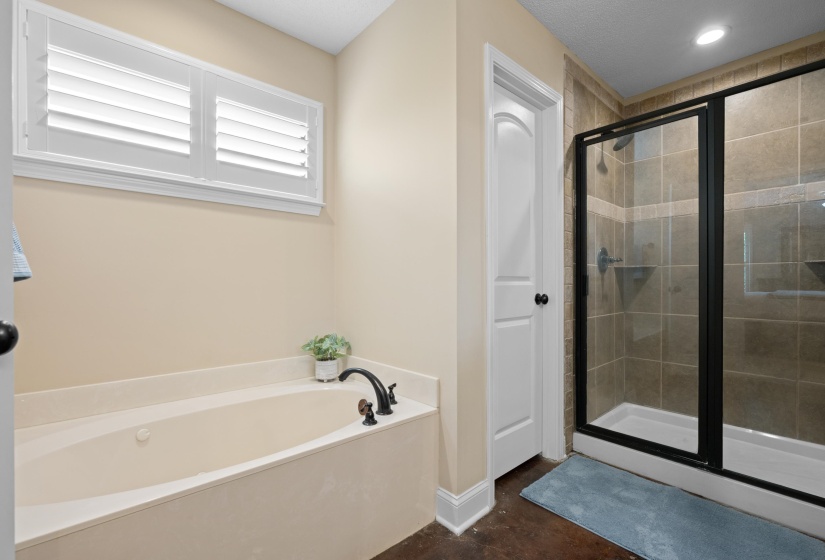 Soaking tub with a dark bronze faucet and a tiled shower enclosure featuring a black frame glass door