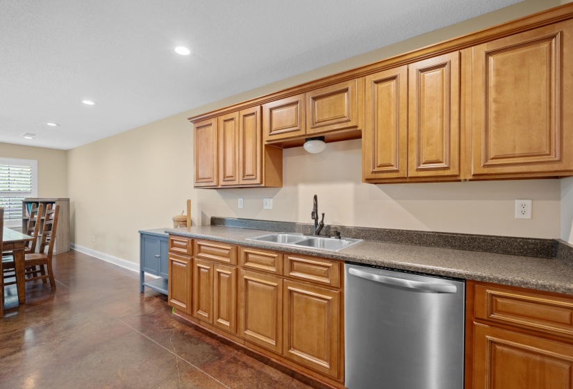 Kitchenette featuring wood cabinetry, stainless steel dishwasher, double basin sink, and laminate countertops