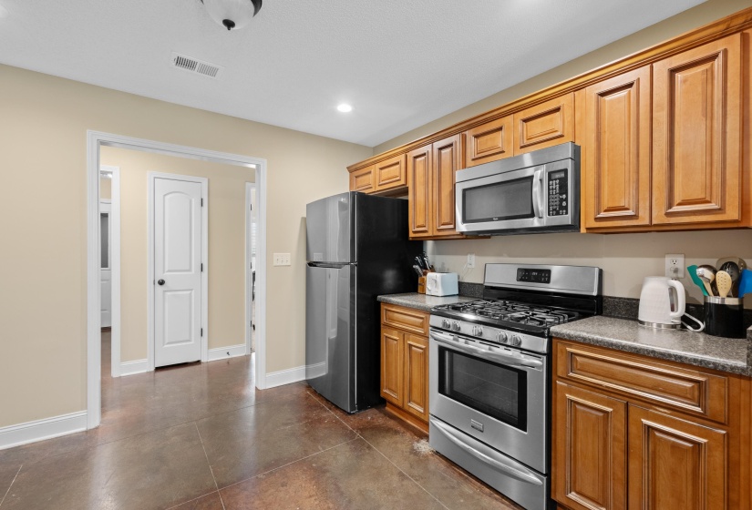 Kitchen featuring wood-finish cabinetry, stainless steel appliances including a microwave and range, dark countertops, and neutral-toned walls