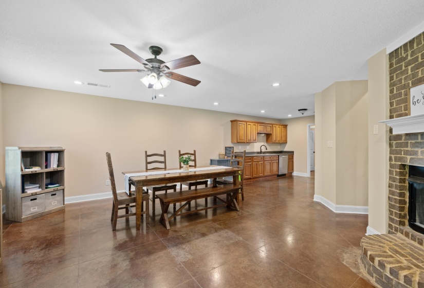Spacious open-concept room featuring a brick fireplace, wood-finish flooring, recessed lighting, and a ceiling fan