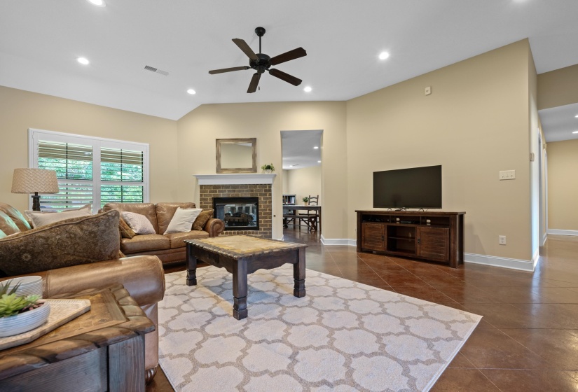 Spacious living area featuring high vaulted ceilings, recessed lighting, a brick fireplace with a white mantel, and wood-finish flooring
