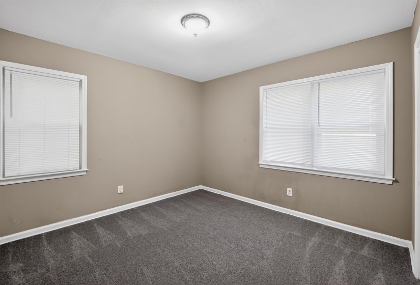 Neutral tone walls featuring two windows with white blinds, white trim, and dark gray carpet flooring
