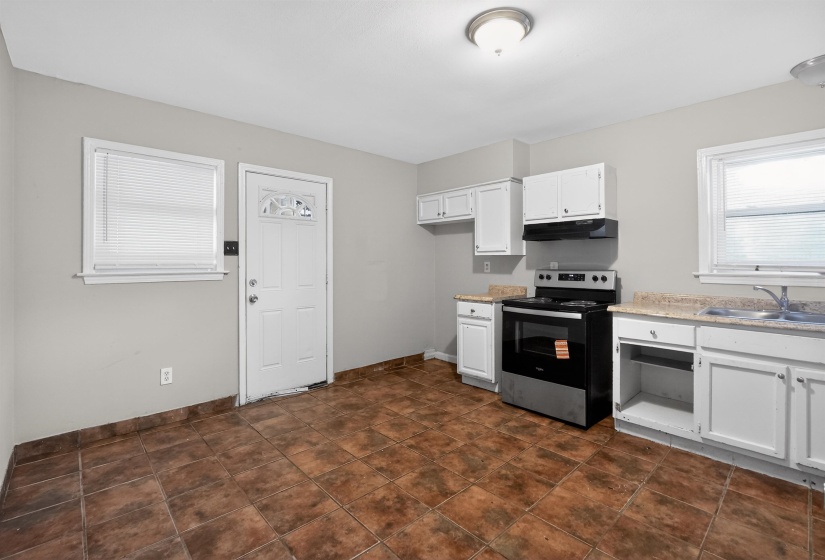 Kitchen area featuring ceramic tile flooring, white cabinetry, laminate countertops, a stainless steel and black range, and an overhead range hood