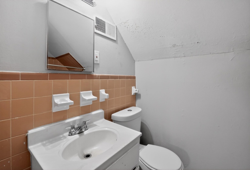 Bathroom featuring a wall-mounted mirror, vanity with an integrated sink, dual-handle faucet, ceramic tile wainscoting, and a white toilet