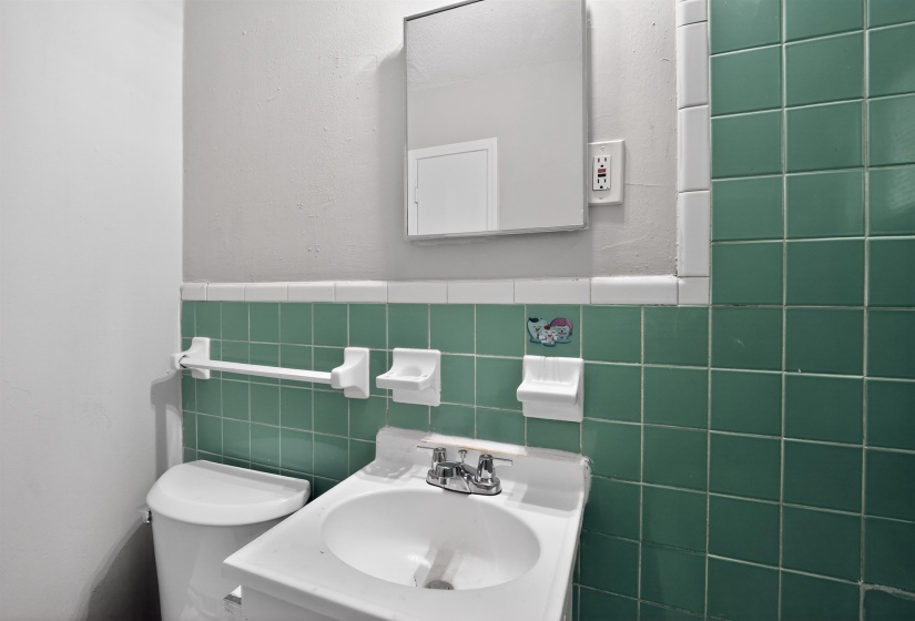 Bathroom featuring green subway tile wainscoting, a wall-mounted sink with chrome fixtures, a medicine cabinet, and a white toilet