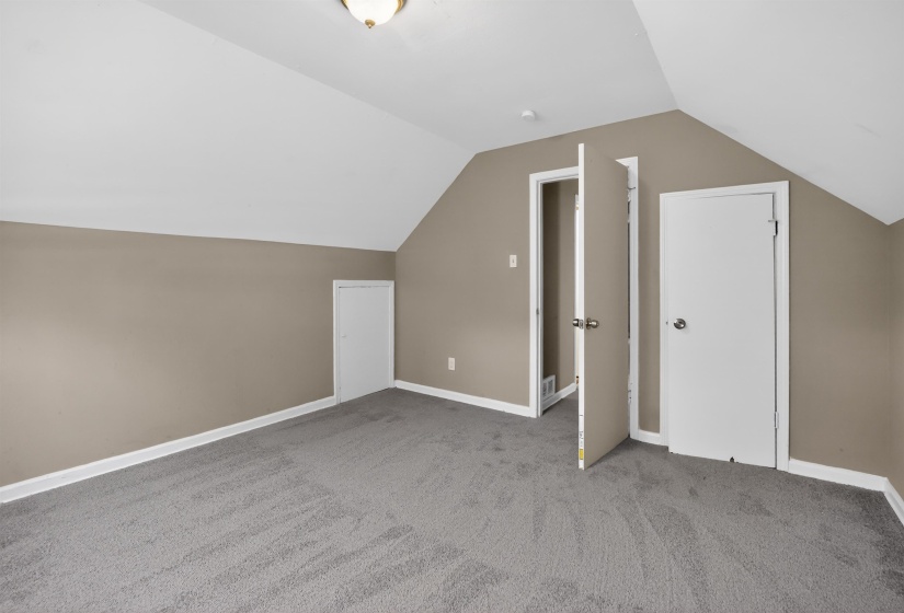 Carpeted room featuring a vaulted ceiling, neutral wall paint, white baseboards, and multiple white doors