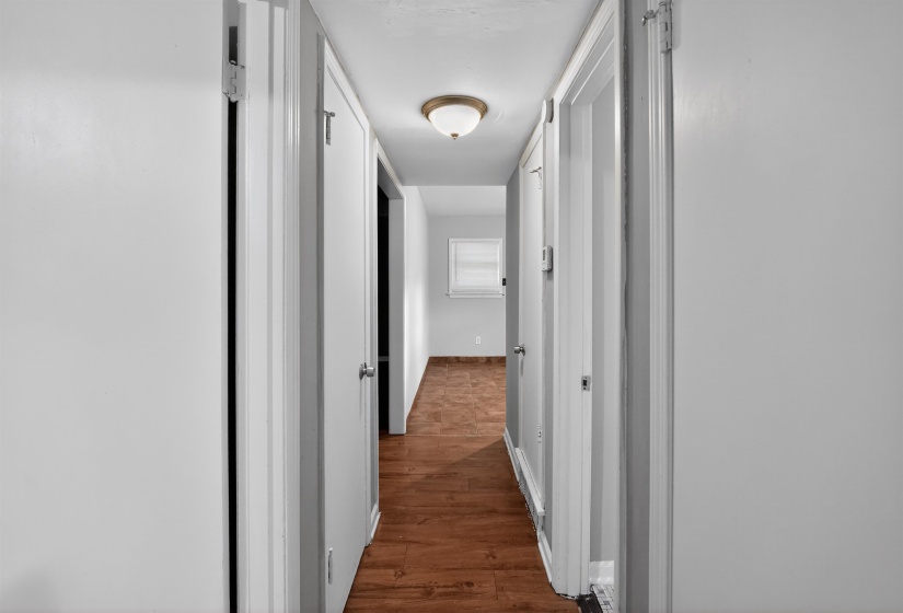 Hallway with wood-finish flooring, white walls, and a ceiling-mounted light fixture