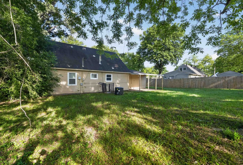 Expansive rear yard featuring green lawn, mature trees, wood privacy fencing, and a covered patio area