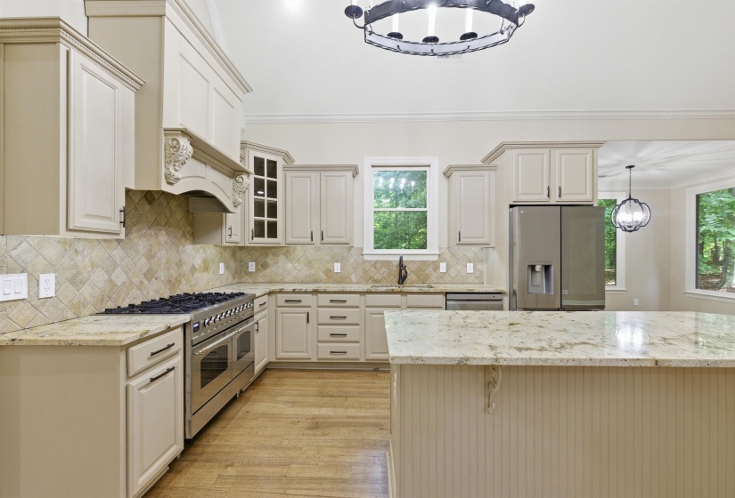 Well-appointed kitchen featuring light-toned cabinetry, a large center island with a stone countertop, a professional-style gas range, stainless steel appliances, and wood-finish flooring