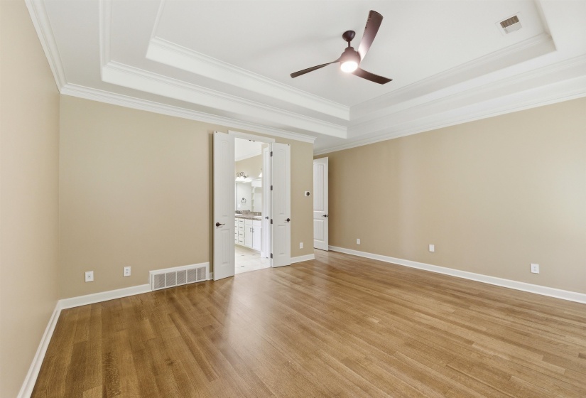 Spacious room featuring wood-finish flooring, a tray ceiling with crown molding, and a ceiling fan