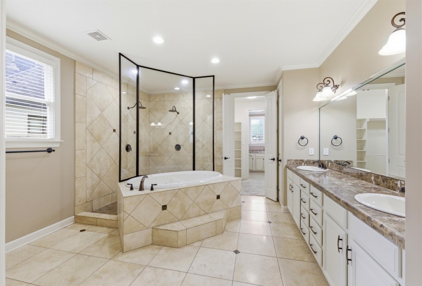 Spacious bathroom featuring a large tiled soaking tub and enclosed shower with multiple showerheads