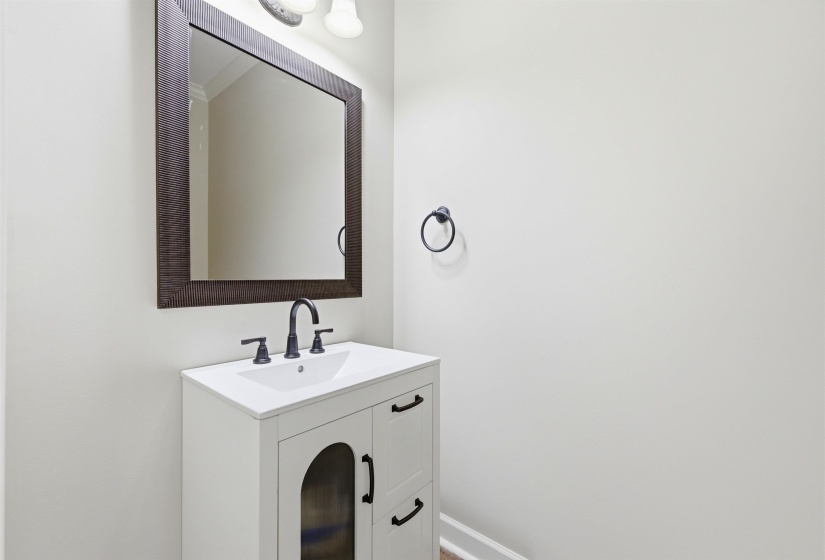 White vanity featuring a single-basin sink, black hardware, and an arched glass door