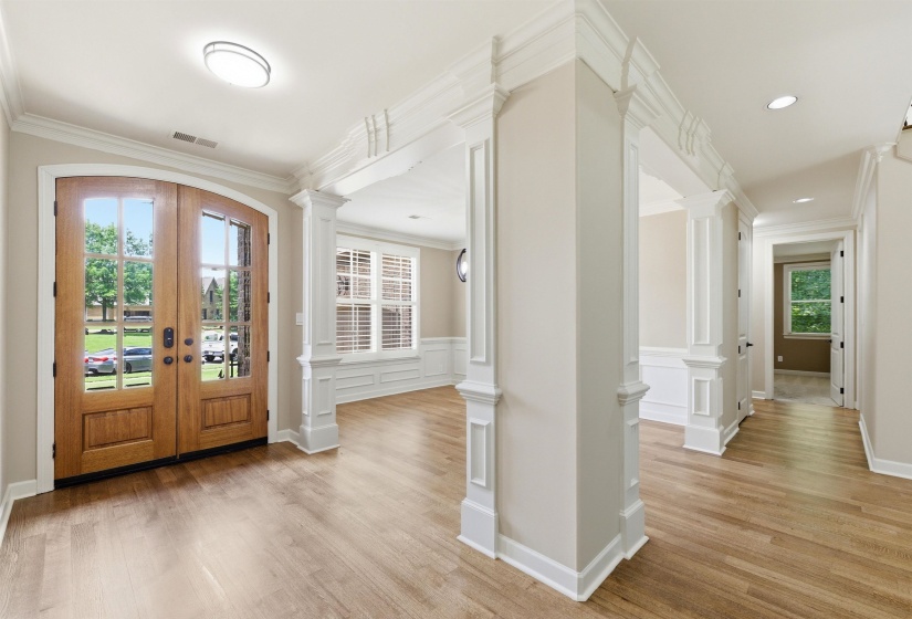 Grand entryway featuring arched double doors with glass panels, wood-finish flooring, and decorative column archways