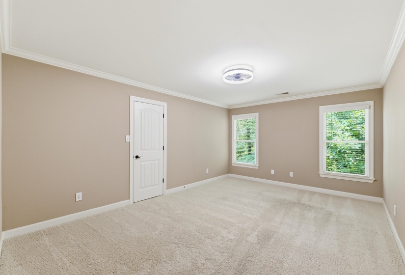 Spacious room featuring neutral carpeting, light beige walls, and crown molding