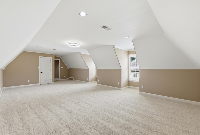 Spacious attic room with neutral carpeting and paint colors