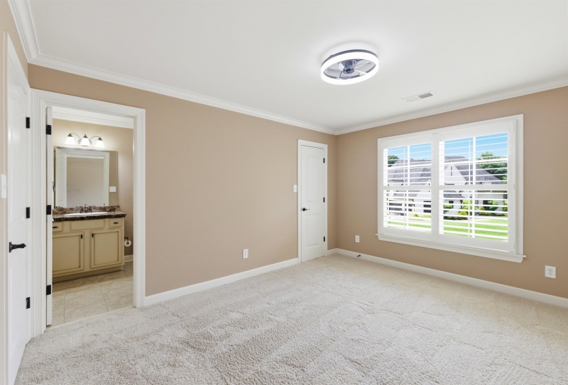 Spacious room featuring light-toned carpet flooring, a multi-pane window with interior shutters, crown molding, and a modern ceiling fan with integrated lighting