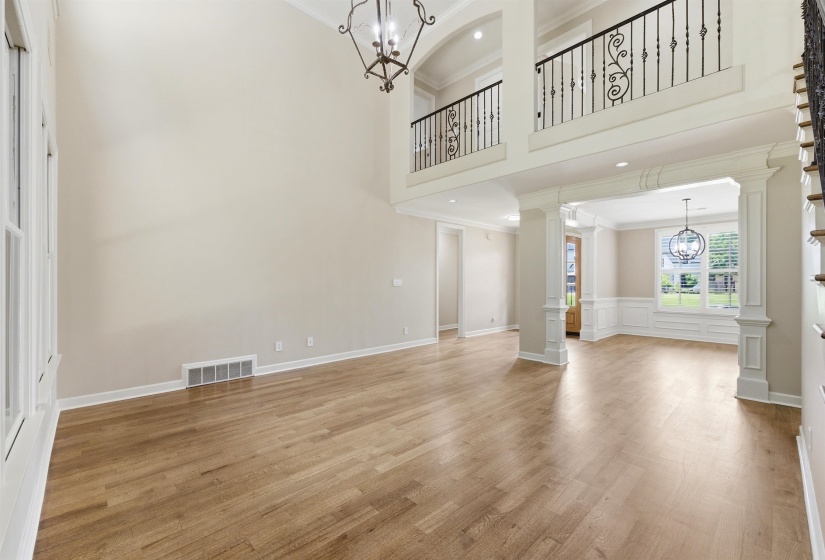 Two-story foyer featuring hardwood flooring, an iron spindle staircase, a wrought iron chandelier, and decorative archways with columns