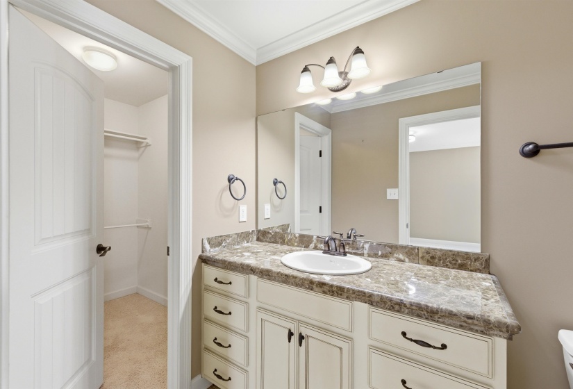 Bathroom vanity featuring a stone-look countertop with an integrated sink, cream-painted cabinetry, and a framed mirror