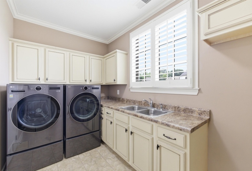 Laundry area featuring ample cabinetry, a double basin sink with countertop space, and window with plantation shutters