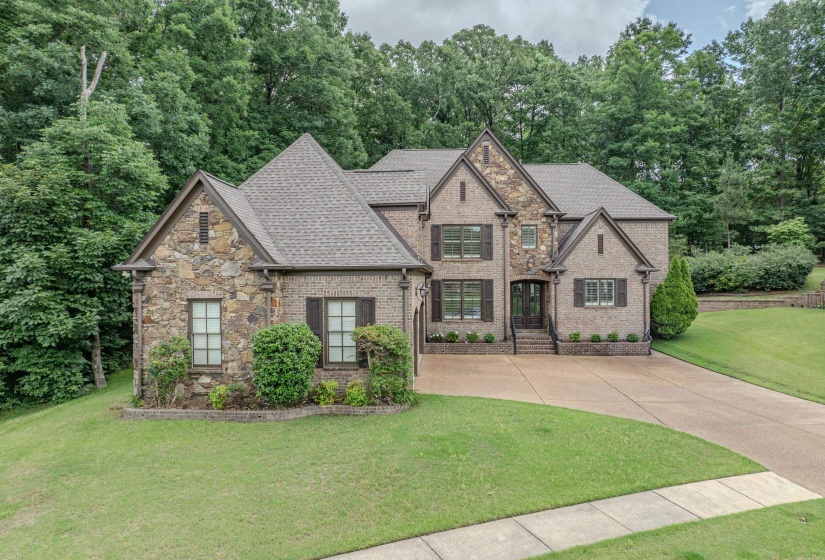 Multi-level brick and stone exterior with dark window shutters, a prominent gabled roofline, and established landscaping