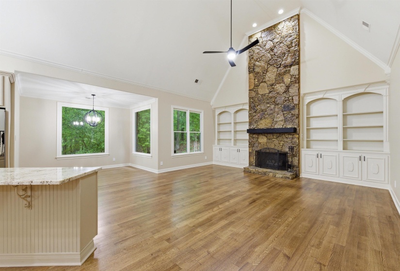 Great room featuring a vaulted ceiling, wood-finish flooring, and a floor-to-ceiling stone fireplace with a dark wood mantel