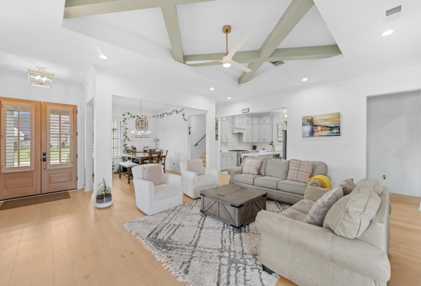 Spacious living area featuring light wood-finish flooring and a prominent tray ceiling with decorative beams