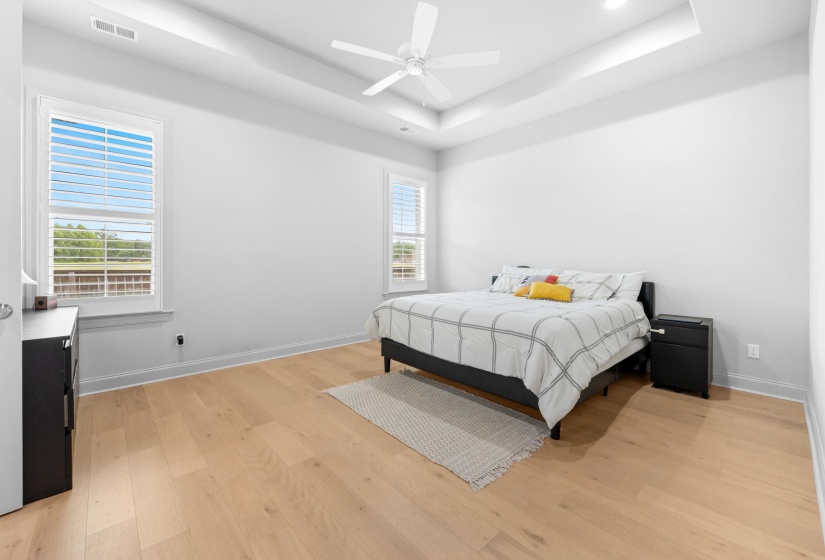 Spacious room featuring light wood-finish flooring, a tray ceiling with a ceiling fan, and recessed lighting