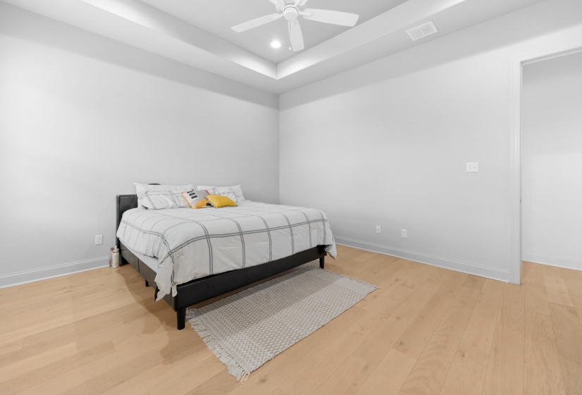 Spacious room featuring light wood-finish flooring, a tray ceiling with recessed lighting, and a ceiling fan