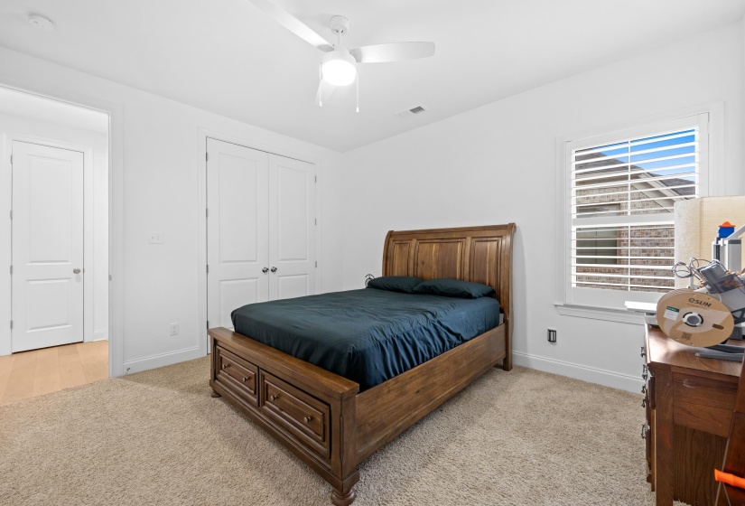 Carpeted room with a ceiling fan, a window featuring white plantation shutters, and a double-door closet with polished chrome hardware