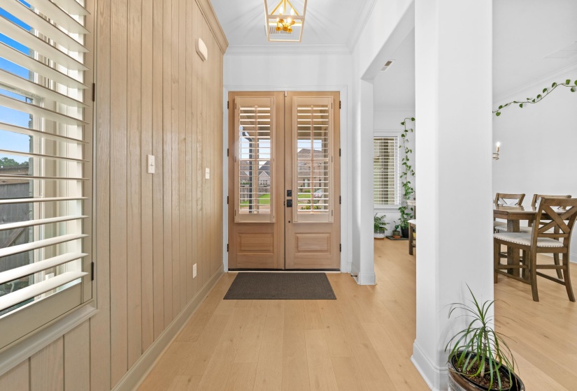 Entryway featuring light wood-finish flooring, vertical wood paneling, and plantation shutters