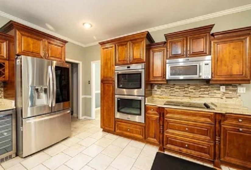 Kitchen featuring warm wood cabinetry, stainless steel appliances including a refrigerator and double wall ovens, granite countertops, and a mosaic tile backsplash