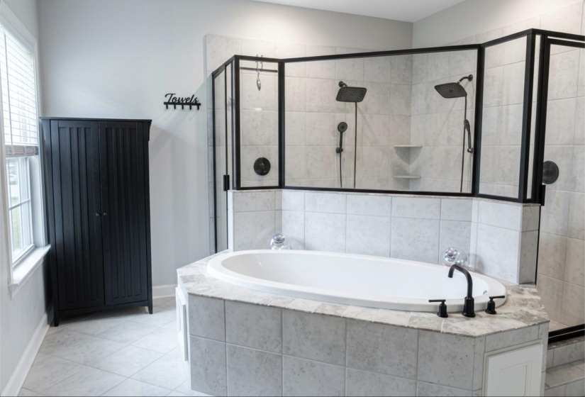 Bathroom featuring a corner soaking tub with a black faucet, a large walk-in shower with dual showerheads and black framed glass enclosure, and light-toned tile flooring