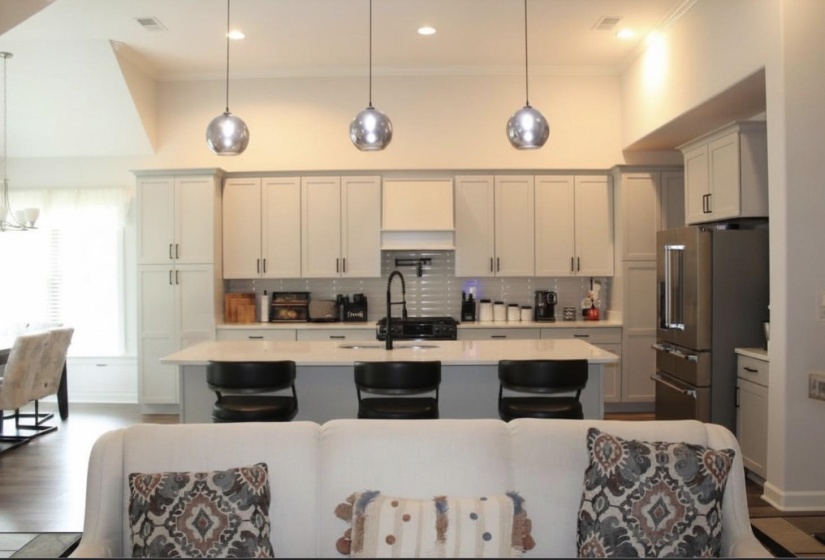 Modern kitchen featuring light cabinetry, a large center island with seating, pendant lighting, and stainless steel appliances