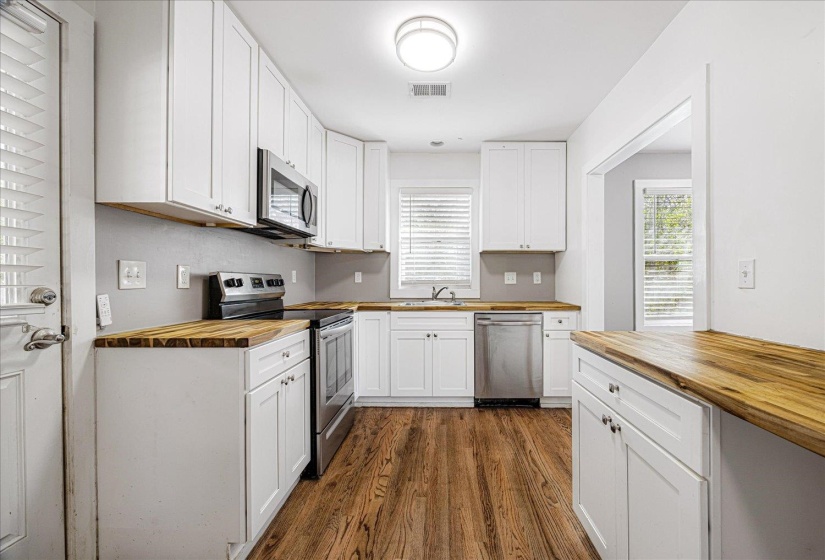 Kitchen featuring wooden counters, stainless steel appliances, white cabinets, dark wood-type flooring, and healthy amount of natural light