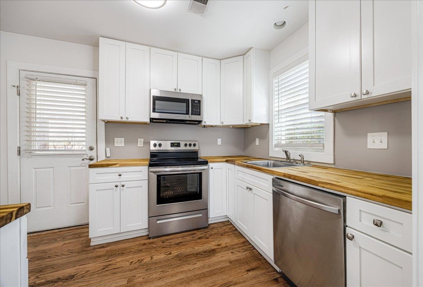 Kitchen with wood counters, stainless steel appliances, white cabinetry, and dark wood-type flooring