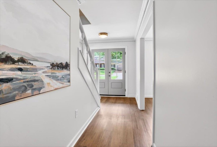 Entryway featuring wood-finish flooring, a white staircase with balusters, and a brass flush-mount light fixture