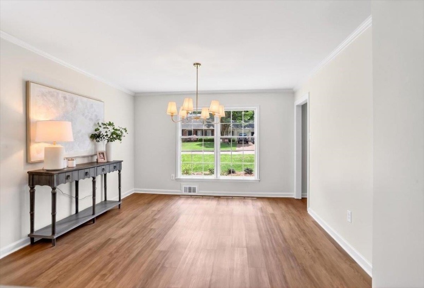 Bright interior space featuring wood-finish flooring, a window with exterior views, crown molding, and a brass-tone chandelier