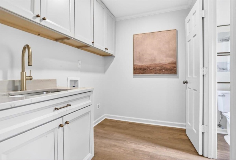 Custom cabinetry with brass hardware, undermount sink with brass faucet, light-toned countertop, and wood-finish flooring