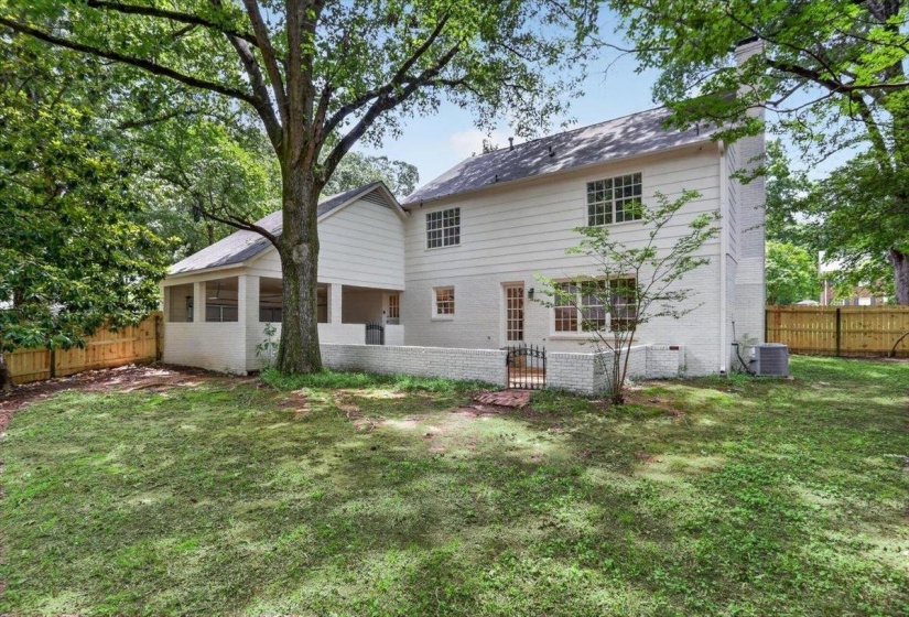 Expansive backyard featuring a manicured lawn, established shade trees, and a screened porch