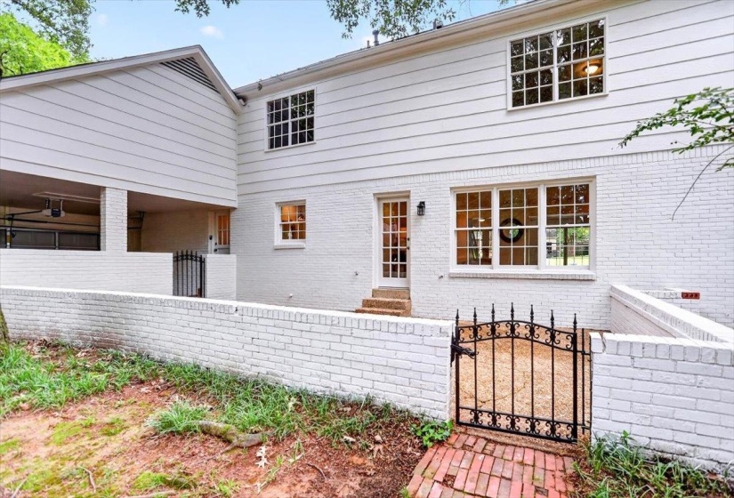 White painted brick and siding exterior featuring multiple windows with grilles, a glass-paned door, and a wrought iron gate