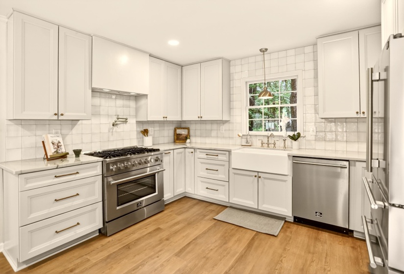 White shaker cabinetry with brass hardware, a farmhouse sink, stainless steel appliances, marble countertops, and wood-finish flooring