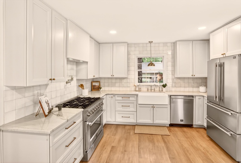 Bright kitchen featuring white shaker cabinetry, stainless steel appliances, light wood-finish flooring, a farmhouse sink, and tile backsplash