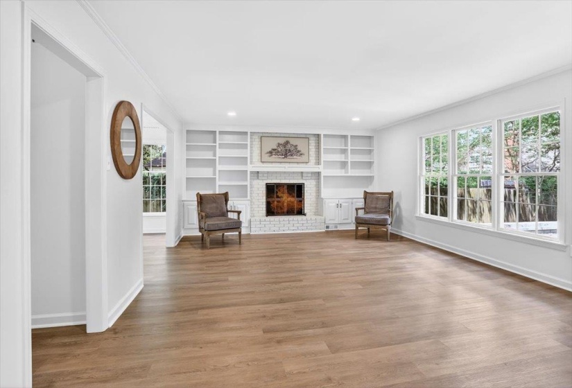 Spacious room featuring wood-finish flooring, a white brick fireplace with built-in shelving, white trim, and multiple large windows