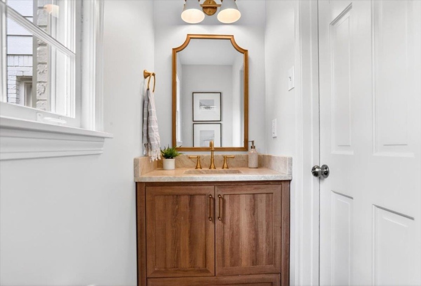Wood-finish vanity with a single basin sink, stone countertop, and gold-finish fixtures