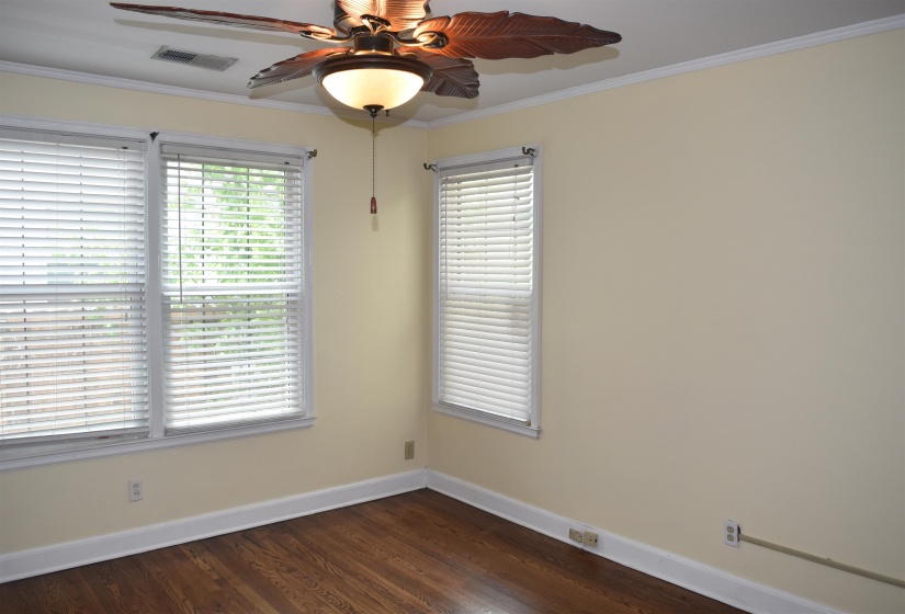 Room featuring wood-finish flooring, two large windows with blinds, a ceiling fan with integrated lighting, crown molding, and neutral wall paint