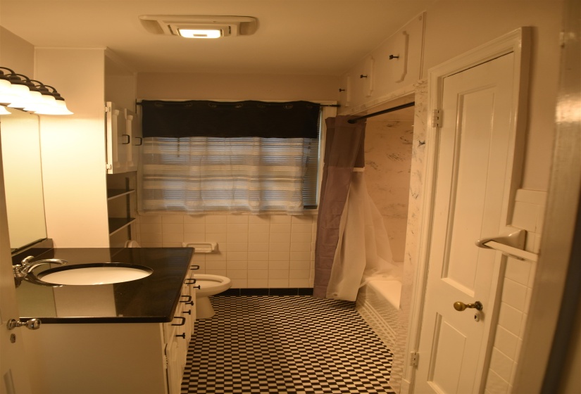 Bathroom featuring checkerboard tile flooring, a dark countertop vanity with an integrated sink, white subway wall tile, and an integrated bathtub and shower