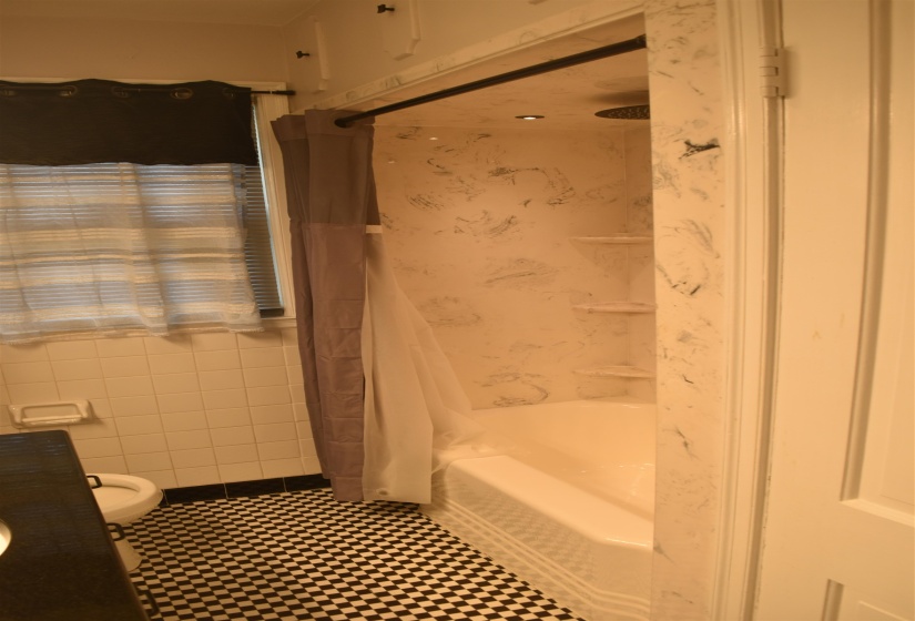 Bathroom featuring a checkered floor, white subway tile walls, and a white bathtub with a marble-patterned surround